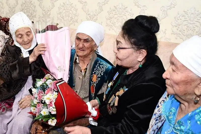 Túrkistandyq 100 jasaǵan ájeler shóbereniń alaqanynan maı jalap, shópshegin erkeletip otyr
