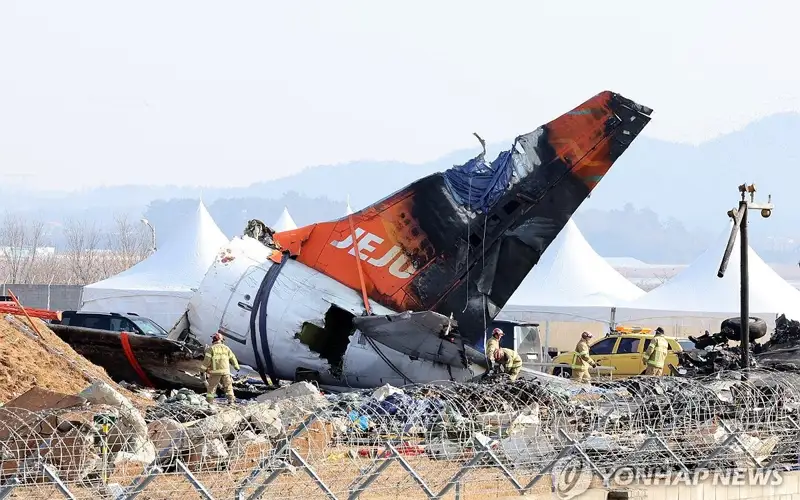 Firefighters remove tarpaulin sheets covering the debris of a Jeju Air passenger plane at Muan International Airport, southwestern South Korea.